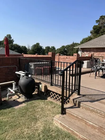Deck stairs with a black metal handrail beside a pool area