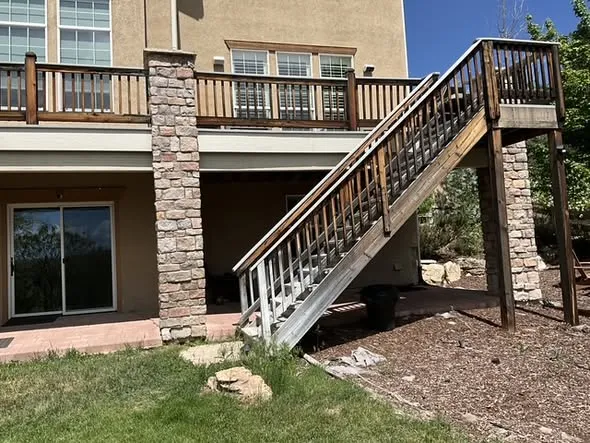 Deck stairs with white balusters beside stone-wrapped support columns