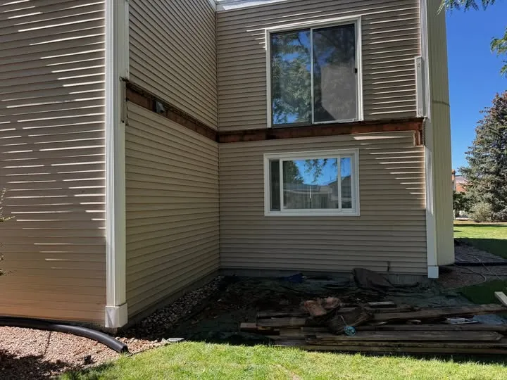 Side of a house after an old deck and ledger were removed, with debris on the lawn