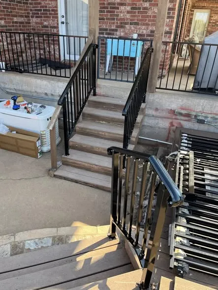 Black metal handrail on deck stairs next to a brick house
