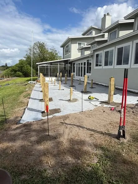 New deck posts standing on fresh footings beside a house during a rebuild